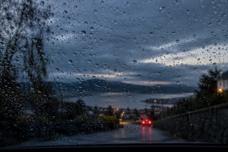 Regentropfen auf einer Windschutzscheibe bei Dämmerung